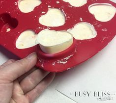 a red heart shaped ice tray with white chocolate chunks in it, being held by a person's hand