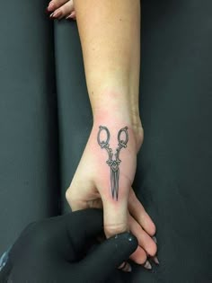 a woman's hand with two scissors on it and a small tattoo design on the wrist