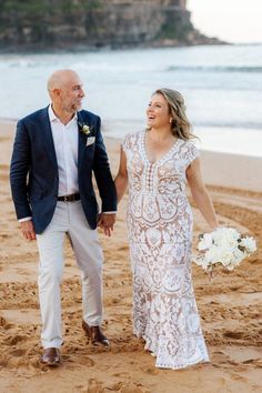 a bride and groom walking on the beach holding each other's hands as they walk towards the ocean