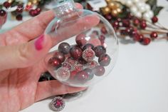 a hand holding a glass ornament filled with red and white balls on top of a table