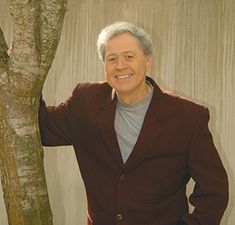 a man standing next to a tree in front of a curtain