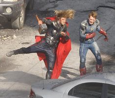 two people dressed as captain america and thor from the avengers movie are running in front of a car