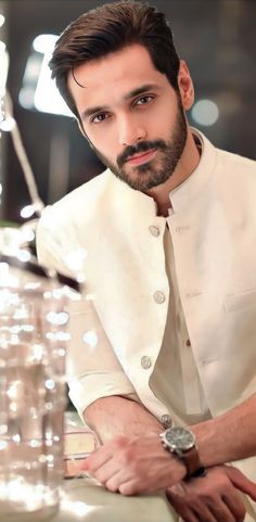 a man with a beard wearing a white shirt and standing in front of a table