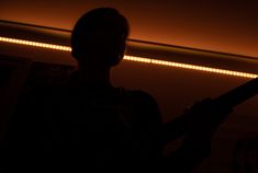 the silhouette of a person holding a guitar in front of a mirror with lights behind them