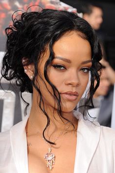 a close up of a person wearing a white shirt and necklace with hair blowing in the wind