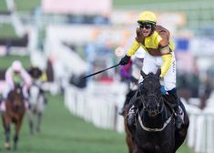 the jockey is riding his horse down the track in front of other horses and spectators