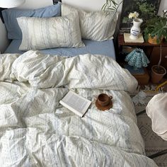 an unmade bed with blue and white comforter next to potted plants on a table