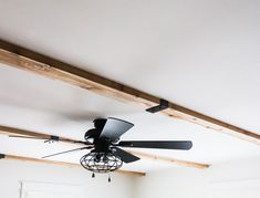 a ceiling fan is hanging from the ceiling in a room with white walls and wood beams