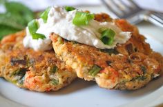 two crab cakes with sour cream and green onions on a plate next to a fork