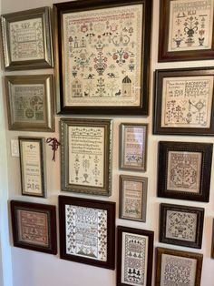 a wall with many framed pictures and cross stitchs hanging on it's side