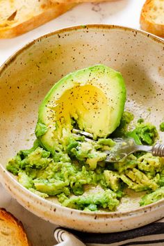 an avocado is being smashed into pieces in a bowl with bread on the side