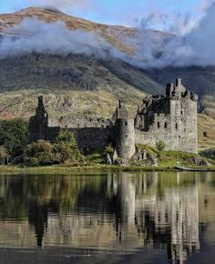 a castle sitting on top of a lush green hillside next to a body of water