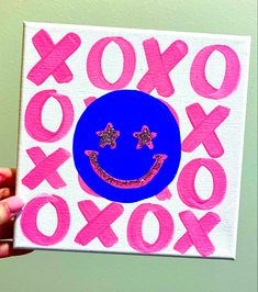 a person holding up a painting with the word xoxo painted on it in pink and blue