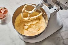 an electric mixer with eggs in it on a counter next to a bowl and spoon