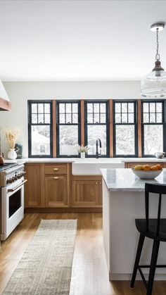 a kitchen with wooden cabinets and white counter tops, an island in front of two windows