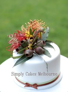 a white cake with flowers and leaves on top sitting on a table in the grass