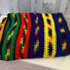 a multicolored crocheted pillow sitting on top of a white table next to a wooden wall