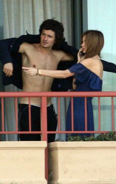 a shirtless man talking on a cell phone next to a woman