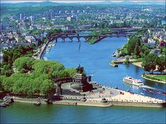 an aerial view of a river and bridge in the city with green trees on both sides