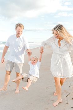 a man and woman holding hands while walking on the beach with a toddler boy