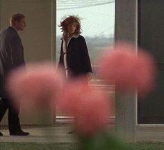 two people standing in front of a door with pink flowers on the ground next to them