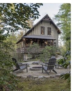 two lawn chairs sitting in front of a wooden house with lights on the porch and windows