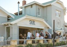 people are standing outside of a restaurant on the side of the road in front of some buildings