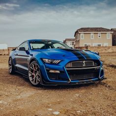 a blue sports car parked in the middle of a dirt field next to some houses