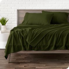 a bed with green sheets and pillows on top of it next to a potted plant