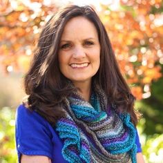 a woman wearing a blue shirt and a multicolored knitted scarf in front of a tree