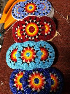 several pieces of beaded art sitting on top of a brown table next to scissors