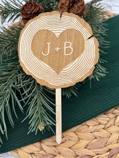 a wooden lollipop with the initials j and b on it sitting next to pine cones