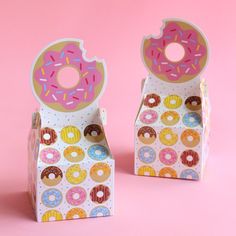 two cardboard boxes with donuts on them are sitting side by side against a pink background