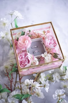 a pink and white flower arrangement in a glass box with a wedding ring inside it