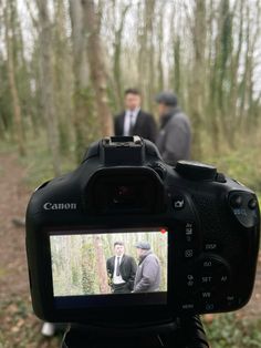 two men are walking in the woods behind a camera