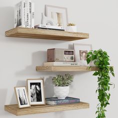 two wooden shelves with pictures, books and plants on them in a corner next to a potted plant