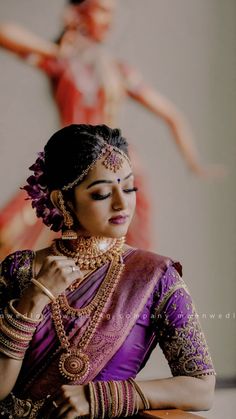 a woman in a purple and gold sari is holding her hands on her chest