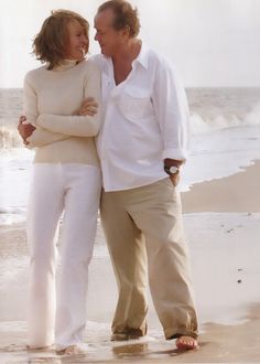 a man and woman standing on top of a beach next to the ocean