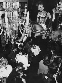 an old black and white photo of people in a room with chandeliers hanging from the ceiling