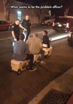 four men sitting on suitcases in the middle of the street at night, with one man talking to another