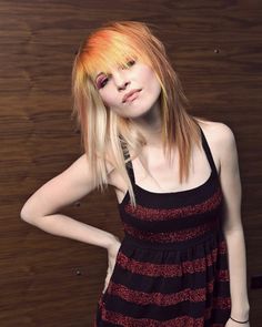 a woman with blonde hair wearing a black and red striped dress standing in front of a wooden wall