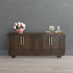 a sideboard with flowers and wine glasses on it in front of a gray wall