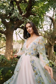 a woman standing in front of some trees wearing a dress with flowers on the side