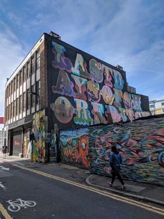 a person walking down the street in front of a building with graffiti on it's side