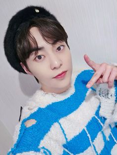 a young man wearing a blue and white sweater pointing at the camera with his finger