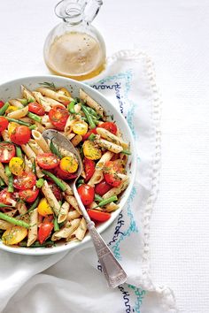 a bowl filled with pasta and vegetables on top of a white cloth next to a spoon