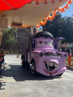 a purple truck with an angry face on it's side and people sitting in the background