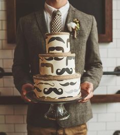 a man holding a cake with mustaches on it