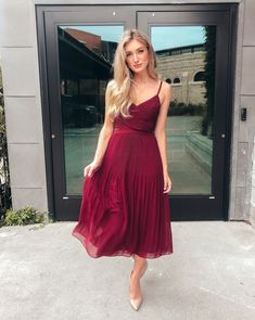 a woman standing in front of a building wearing a red dress