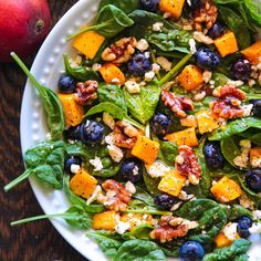 a salad with blueberries, spinach and walnuts in a white bowl on a wooden table